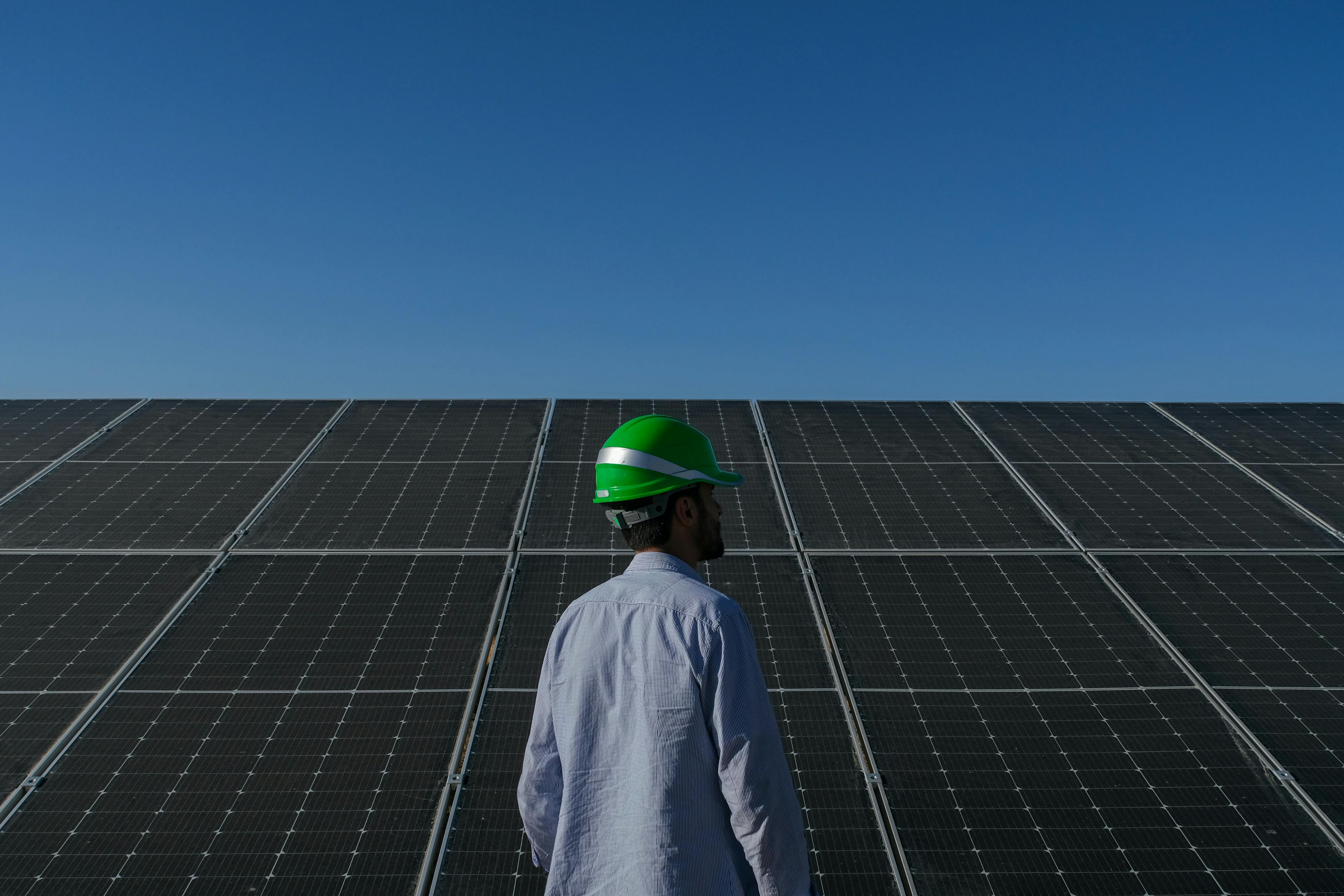 Energy industry worker in hard hat standing in front of solar panels