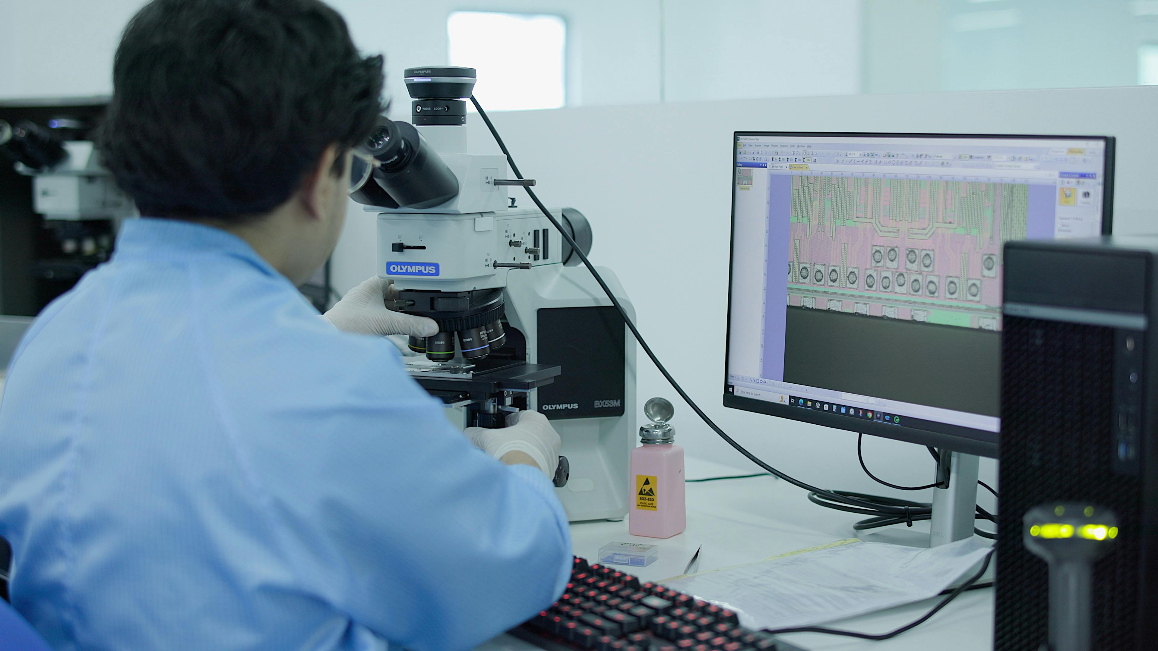 A Fusion Worldwide engineer examining a sample under a microscope at their desk
