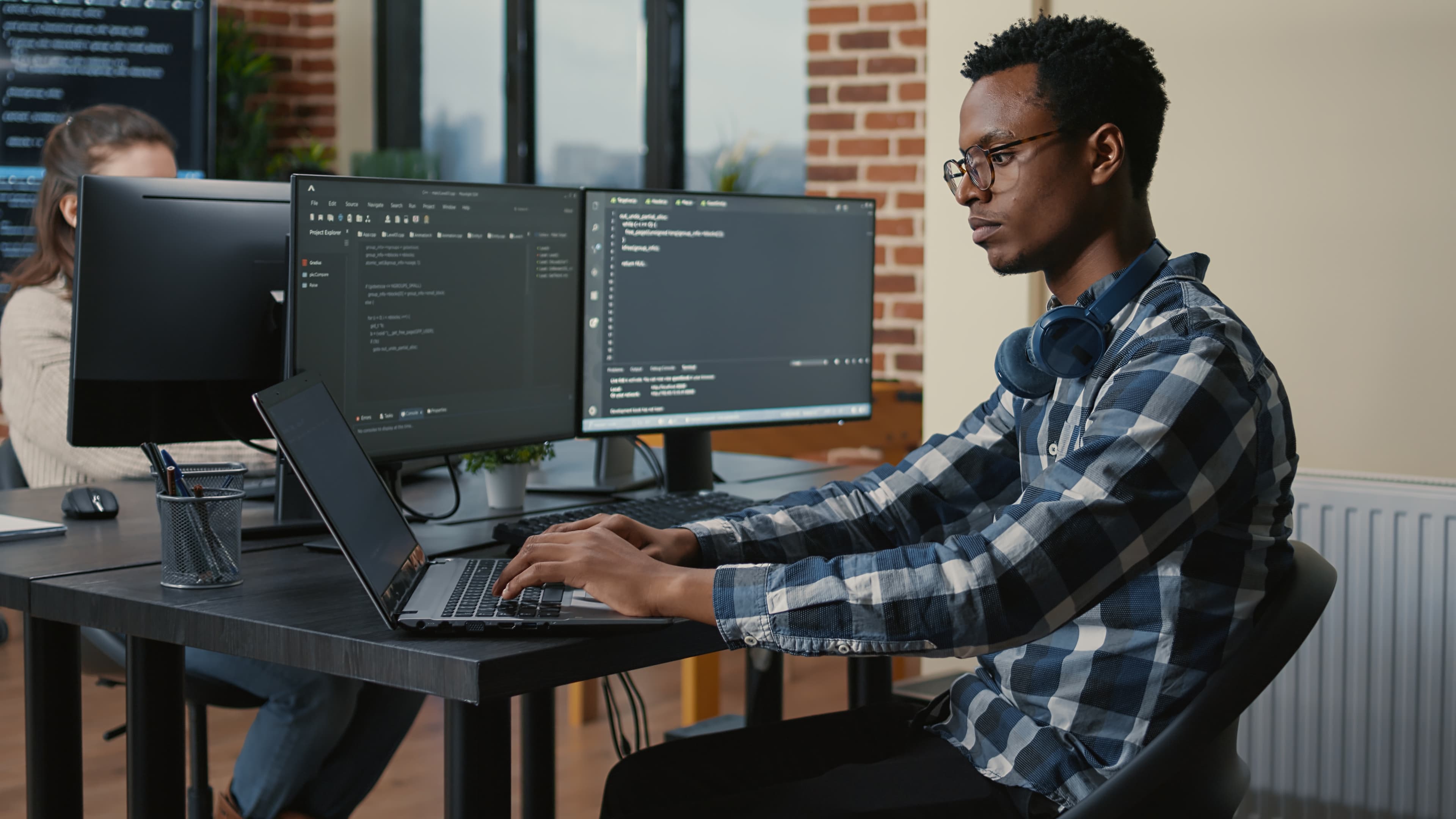 Person typing on a laptop in front of two additional monitors