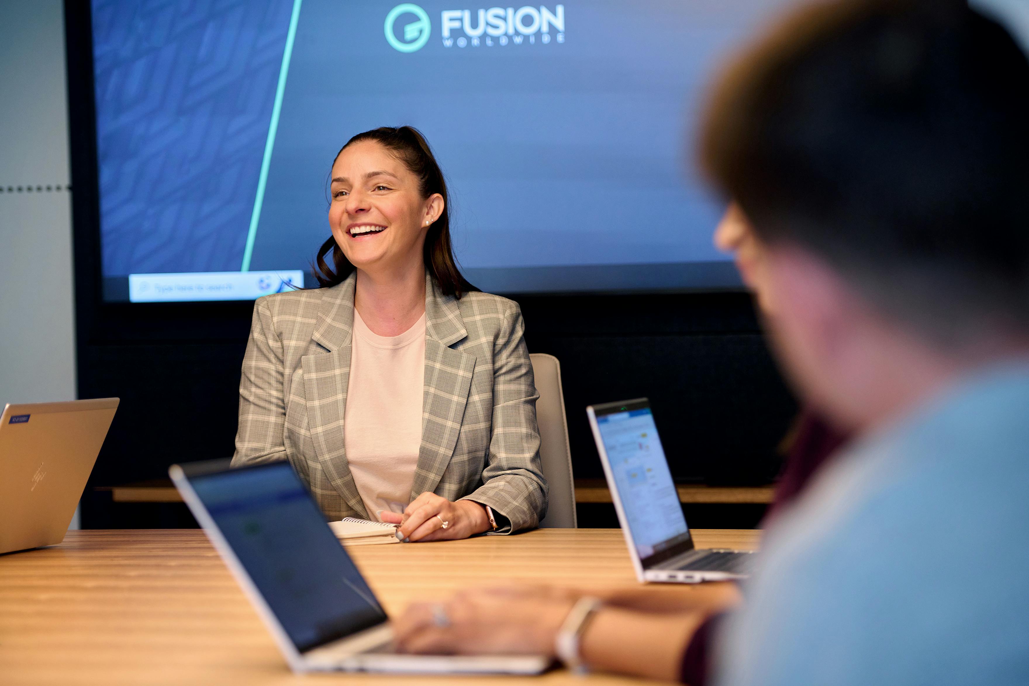 A bright young Fusion employee laughs joyfully, seated at the head of a conference room table