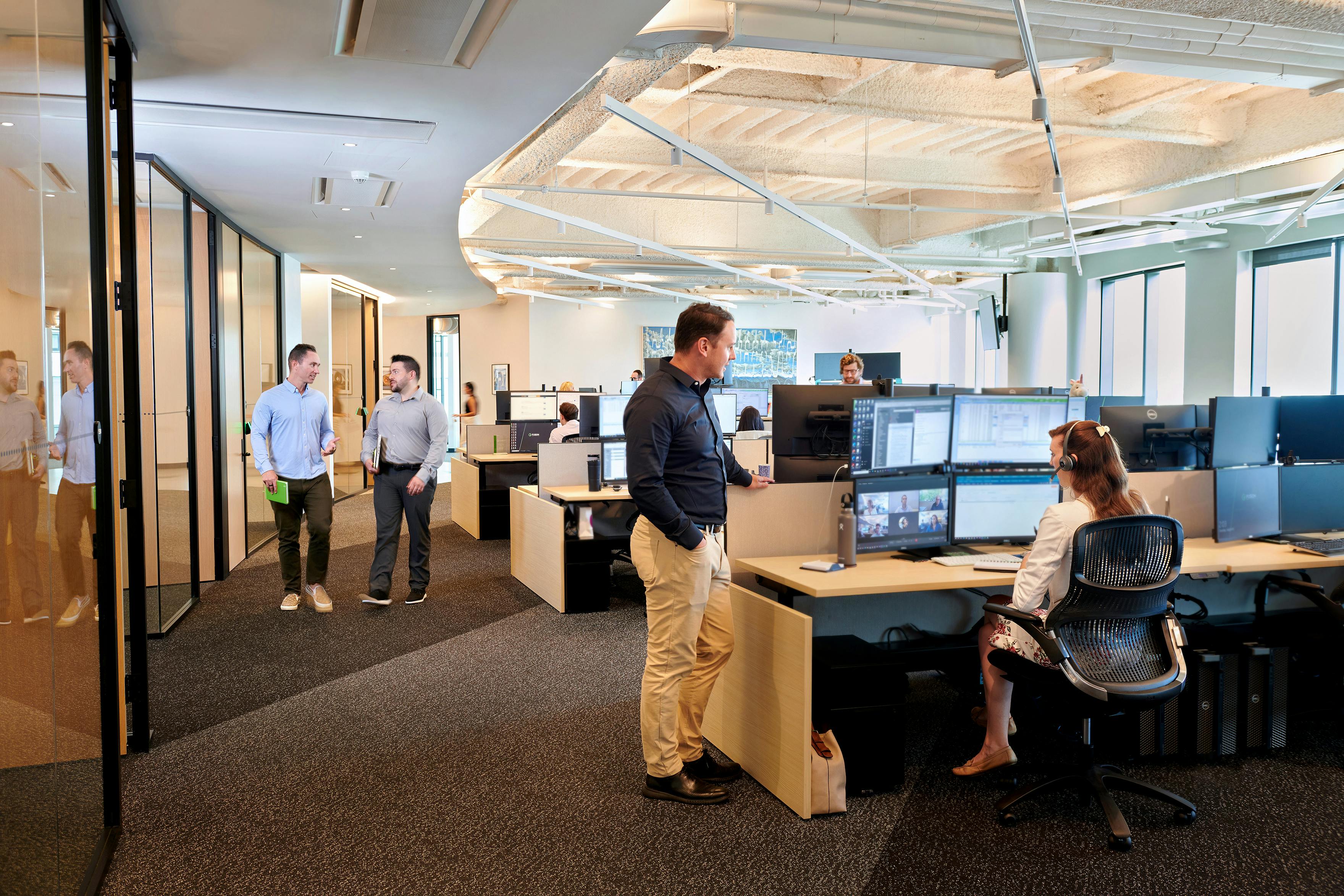 A modern office interior with employees chatting, walking, and working at desks
