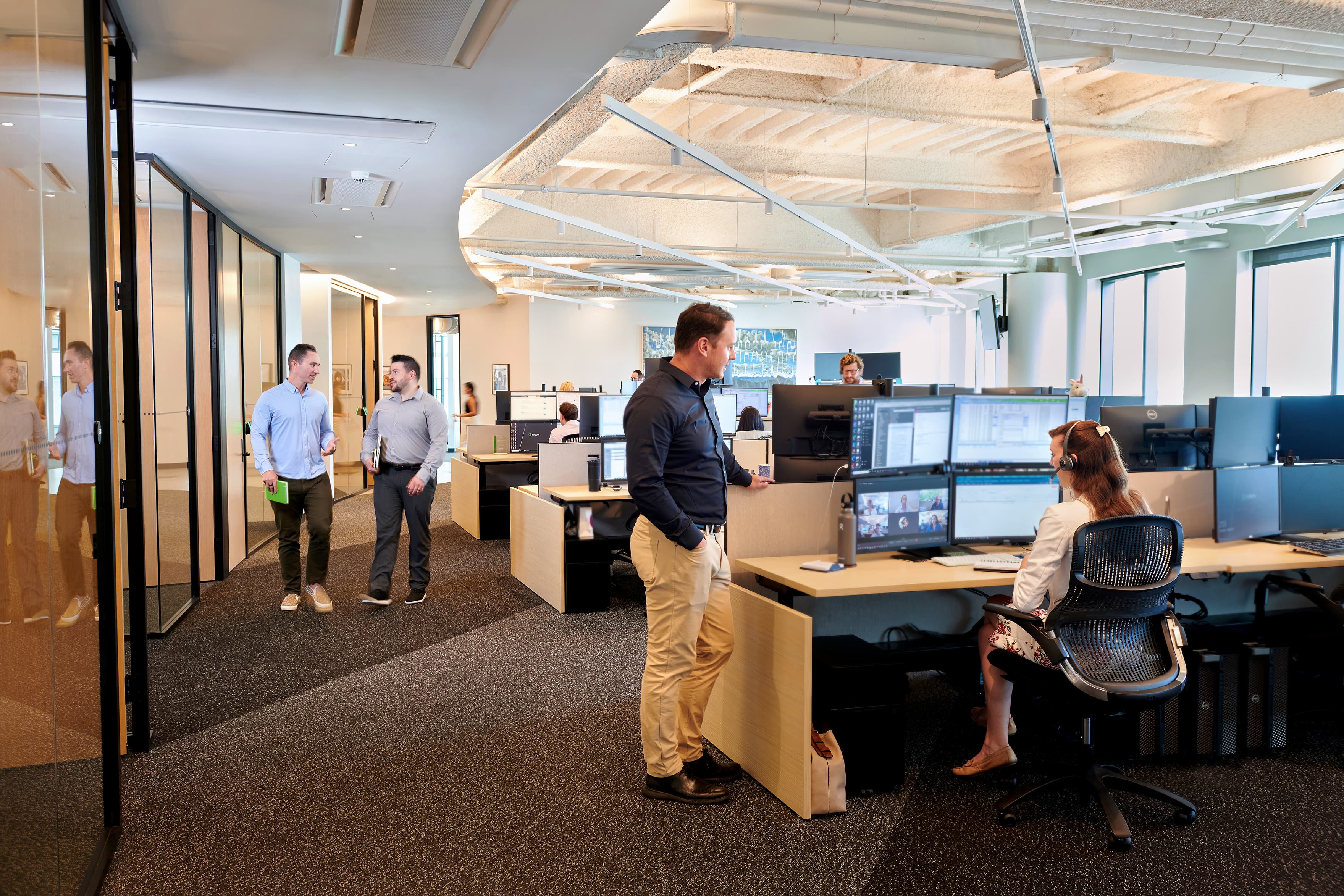 A modern office interior with employees chatting, walking, and working at desks